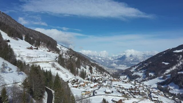 Amazing drone flight of a stunning alpine valley, village and snow covered mountain peaks in Champery, Switzerland. A beautiful winter wonderland scenic flight on a clear blue sky day.