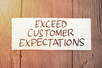 Exceed customer expectations, text words typography written on paper against wooden background,...