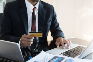 Male businessmen use credit cards to conduct financial transactions through phones, tablet, and laptop at home office.