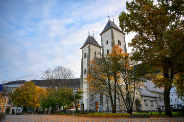 Fototapeta na wymiar In front of St.Mary's Church in autumn In the foreground there were many dry leaves on the rocky road, on a blue sky day. In Bergen, Norway
