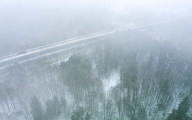 asphalt road through a snow-covered forest in dense fog. winter foggy nature landscape. aerial view