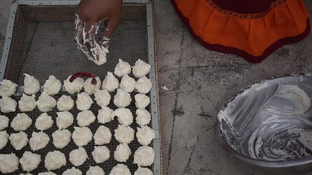 Indian woman is preparing Daler bori on a net in sunny day. It is a form of dried lentil dumplings popular in Bengali cuisine.