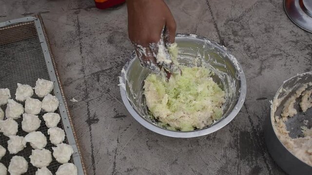 Indian woman is preparing mixture Daler bori in a bowl in sunny day. It is a form of dried lentil dumplings popular in Bengali cuisine.
