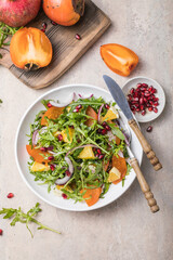 Delicious persimmon salad with arugula  and orange served on light grey table, flat lay. Space for text