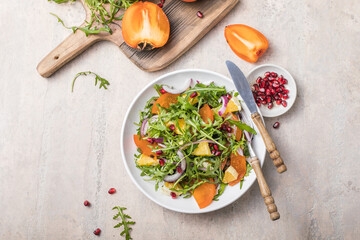 Delicious persimmon salad with arugula  and orange served on light grey table, flat lay. Space for text