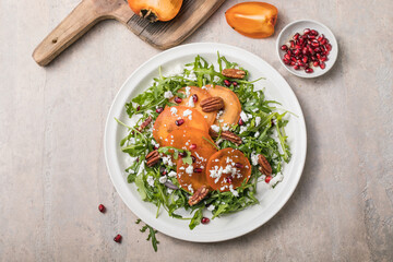 Persimmon salad with arugula, nuts, goat cheese, pomegranate. Healthy vegetarian food concept.