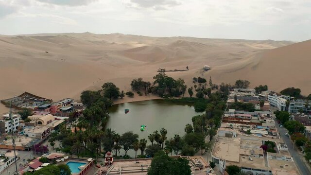 Aerial shot rising above the small village of Huacachina in Peru, showing the water oasis surrounded by desert.