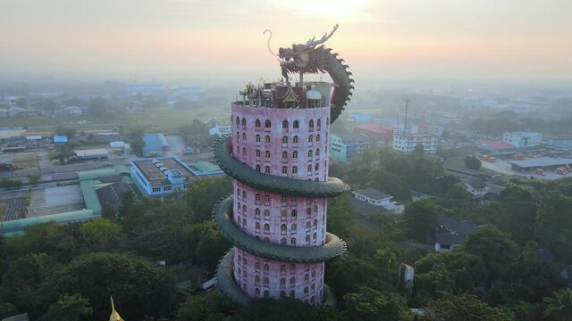 4k Sunrise Cinematic footage panning around The Wat Samphran Temple with huge dragon coiled around and protecting it in Amphoe Sam Phran province in Bangkok, Thailand. Aerial revealing Dragon temple
