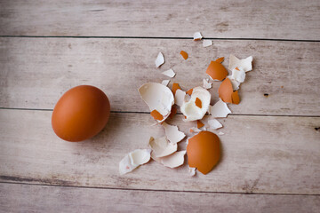 One whole chicken egg and the remains of a shell on a wooden background