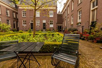 Close up image of rustic metal chair and table at acourtyard garden in a senior housing community. In the background there is  a well maintained garden, brick buildings and cobblestone ground.