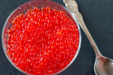 Red caviar in glass jar with silver spoon . Sea food. Healthy eating. Diet. black background.