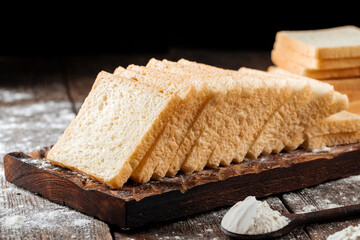 Sliced white sandwich bread on a wooden cutting board with flour