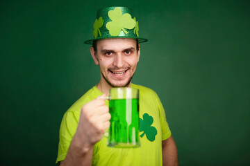 A man in a shamrock hat and green T-shirt drinks a large mug of green ale. Guy celebrates st...