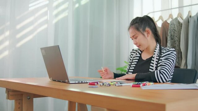 Busy working Asian work concentration focused on working researching data writing on note book and online internet, fashion sales marketing using laptop computer at home modern office workstation desk