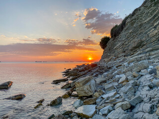 the setting sun on the sea rocky shore in the sea a large triangular shaped stone on a wild beach