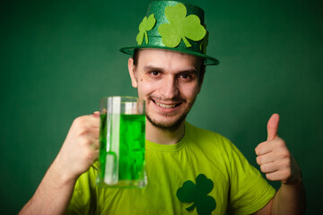 A man in a shamrock hat and green T-shirt drinks a large mug of green ale. Guy celebrates st...