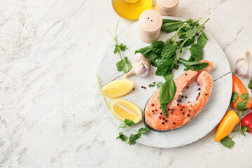 Plate with raw salmon steak, herbs and spices on light background