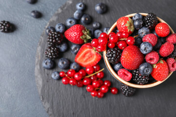 Bowl with different ripe berries on dark background