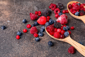 Spoons with different frozen berries on grunge background