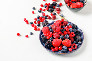 Bowls and spoon with different frozen berries on white background