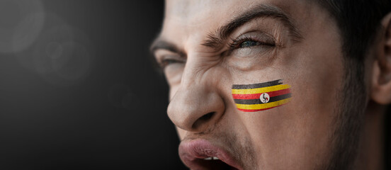 A screaming man with the image of the Uganda national flag on his face