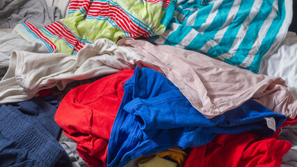 A pile of un-ironed clothes of various colors lies on the floor.