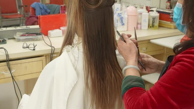 This video shows a hair stylist in a face mask taking the first cuff off of a woman's long hair.