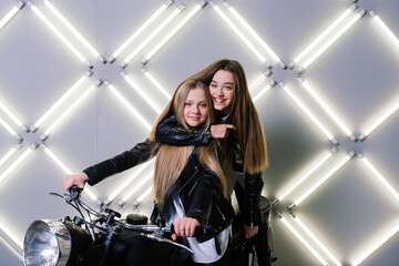 Plakat Two beautiful girls wearing costumes of racers and sitting on a motorcycle, in the studio