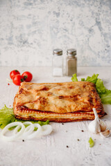 Pie with potatoes and chicken, with onions, peppers, mushrooms lies on a lettuce leaf and light background