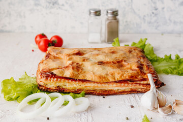 Pie with potatoes and chicken, with onions, peppers, mushrooms lies on a lettuce leaf and light background