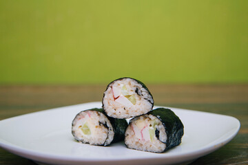 Hand with Chinese chopsticks beats homemade sushi rolls. Rice and fish wrapped in nori seaweed on a white plate.