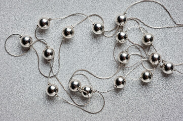 Women's jewelry in the form of silver beads on a silver thread with a clasp, photographed against a silver background.