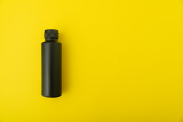 Black bottle vial on yellow background. Copy space. Mock up.