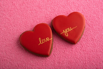 Two red cookies in shape of hearts with the inscription LOVE YOU. Pink background.