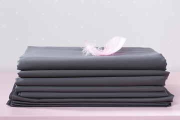 On the table is a stack of folded blank gray sheets with a pink feather.