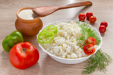 Rustic cottage cheese in white bowl with fresh vegetables on the kitchen table. Appetizer of tomatoes, peppers, cottage cheese, sour cream and spices.