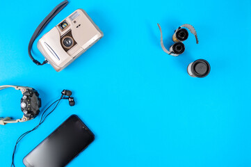 An old camera with film, a watch, headphones, and a smartphone on a flat layer. Retro and travel themes on a blue flat layer