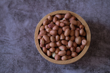 Raw Groundnuts in the wooden bowl on cement background. Top view. 