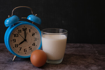 Close up a glass of milk and egg in front of the blue vintage alarm clock. 8.00 o'clock morning...