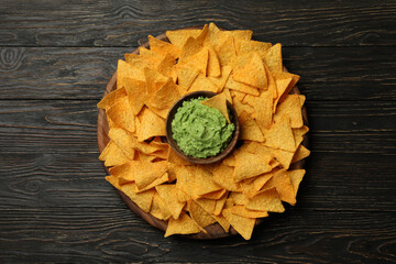 Tray with chips and bowl of guacamole on wooden background, top view