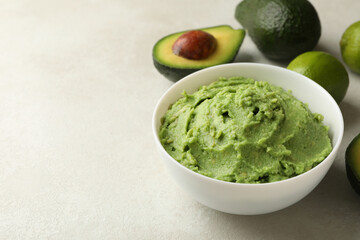 Bowl of guacamole, avocado and lime on white textured background, space for text