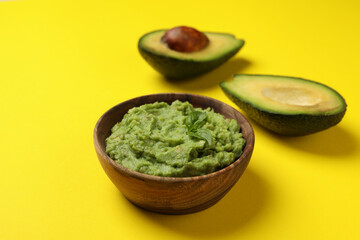 Bowl of guacamole and avocado on yellow background