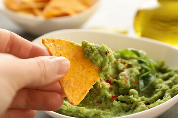 Female hand dips chips slice in guacamole, close up