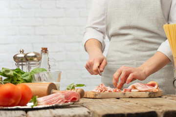 Chef cooks in a light kitchen. Cuts pieces of bacon, on a background with ingredients. Cooking and recipe book, hotel and restaurant business