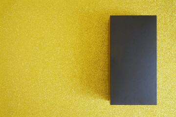 A black paper rectangular box lies on a shiny golden background. A surprise gift for a man. The...