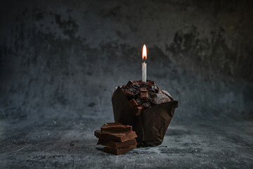chocolate muffins on a dark background with a lit candle