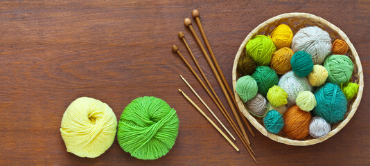 Fototapeta na wymiar Beautiful composition with accessories for hand knitting: balls of colorful yarn in basket, knitting needles and crochet hooks on wooden background. Needlework and hobby. DIY concept. Flat lay, mockup