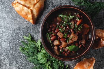 Bean soup with herbs in a clay bowl with fresh rye bread and garlic on a slate table on a dark background.