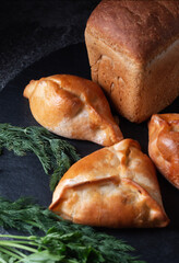 Fresh baked goods. Rye bread with meat patties and greens on a slate table on a dark background