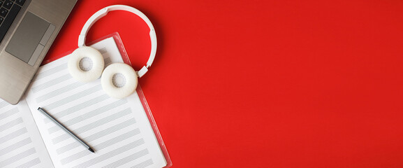 Top view open music book, headphones pen and laptop on red background. workplace. banner